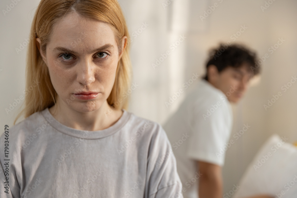 Obraz premium Upset young woman staring at camera after relationship conflict with boyfriend. Concept of emotional stress, couple argument, breakup, trust issues in romantic relationship.