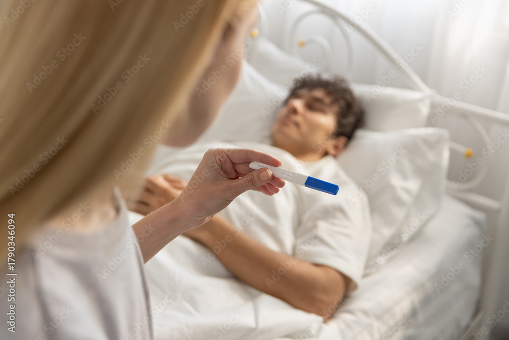 Obraz premium women holding pregnancy test while looking at sleeping boyfriend in bed. Concept of unexpected news, pregnancy result, family planning, relationship decision, surprise, emotional moment.