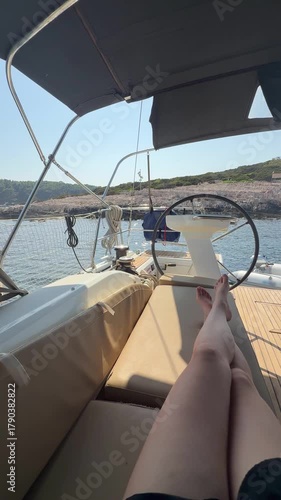 Bare legs of a woman relaxing in the cockpit of a yacht at anchor in a remote bay. Peaceful sailing getaway in wild nature with sea view and summer freedom.