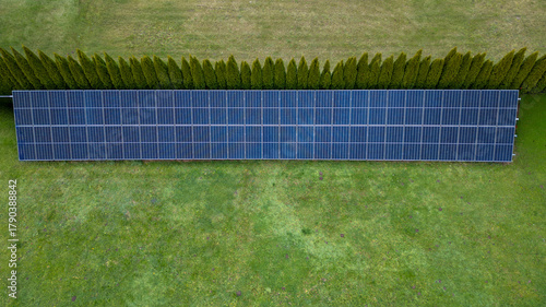 Aerial view of solar panels on a lawn bordered by dense green shrubs; sustainable energy.