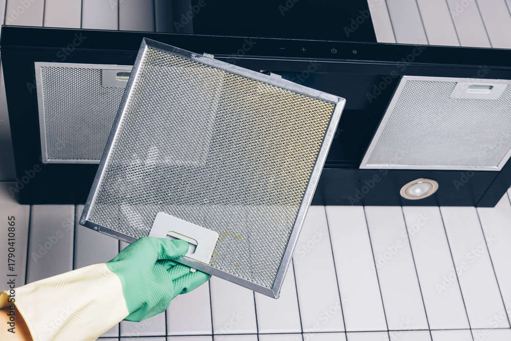 Naklejka premium Woman's hand removing a filter from cooker hood for cleaning or service. Replacing filter in kitchen hood. Professional cleaning kitchen hood with rag