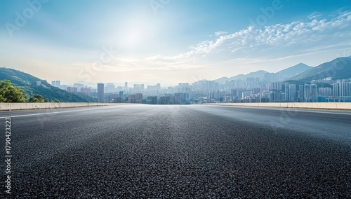 A serene urban landscape featuring a smooth asphalt road leading towards distant mountains and a skyline under a bright blue sky.