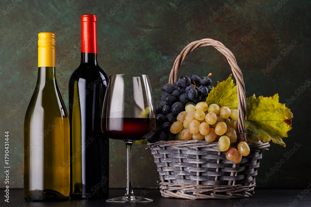 Naklejka premium Red and white wine bottles with a glass and basket of fresh grapes