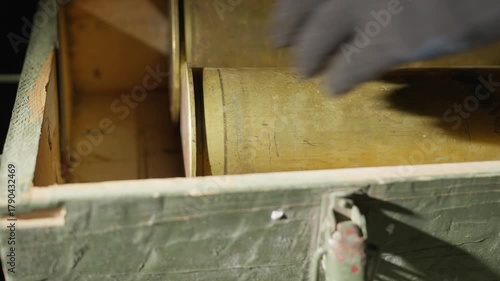 Man in black protective gloves closes the lid of an old military ammunition box after placing an artillery shell inside. Vintage green crate with metal latch under warm cinematic light. 4K close-up.