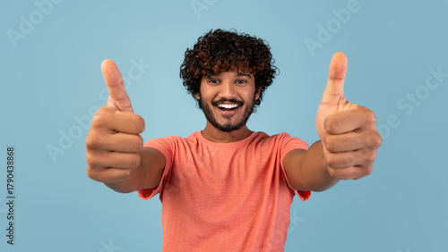 Canvas Print A handsome young eastern guy in a pink t-shirt poses alone against a blue background