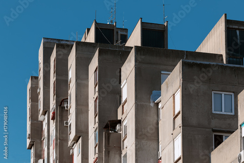 High-rise brutalist concrete apartment building in Belgrade with staggered balconies against a deep blue sky.