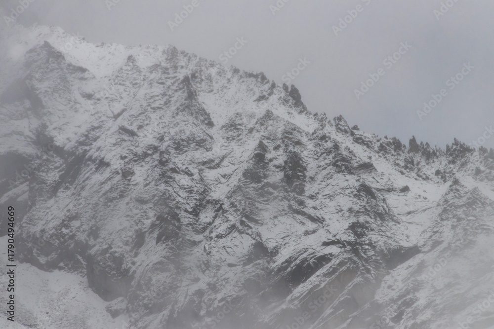 Obraz premium Snow covered rocky mountain ridge in misty winter landscape with dramatic texture and cold atmosphere
