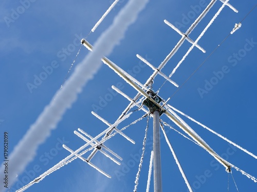 A close-up shot of a high VHF radio antenna with stay ropes covered in snow against blue sky