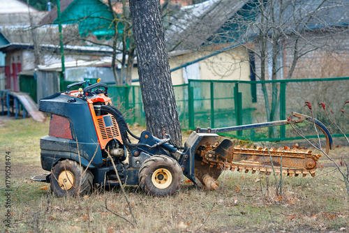 Photography Walk-behind trencher parked in rural yard near tree prepared for digging, soil maintenance work in countryside environment