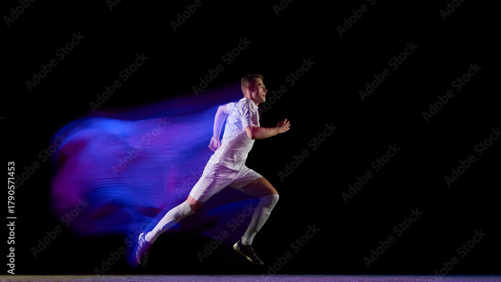 Naklejka premium Soccer runner sprinting with purple blue trail effect on black background. Concept of physical energy, endurance, and motion technology for sportswear and performance brands.
