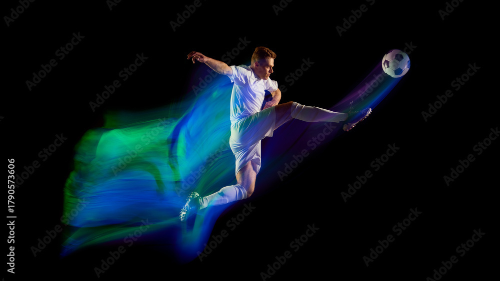 Fototapeta premium Soccer player jumping and kicking ball with green and blue neon motion trail. Concept of precision, performance, and courage used in athletic campaigns and creative design visuals.