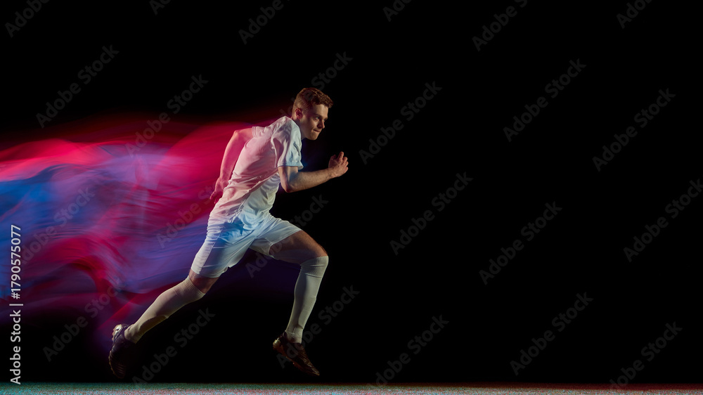 Naklejka premium Football player running fast with glowing red and blue motion blur in dynamic action. Concept of endurance, focus, movement used in athlete training, advertising, and sports analytics.