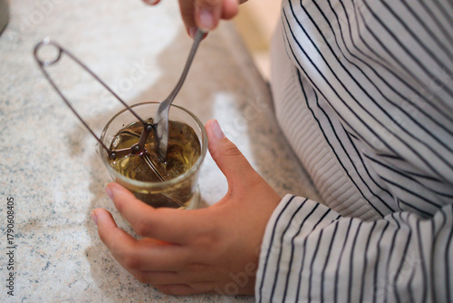 Preparing herbal tea with a metal infuser in a glass cup