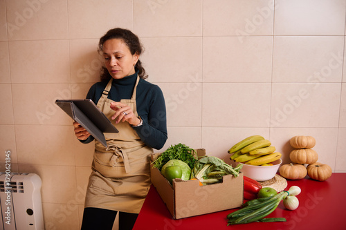 Obraz na płótnie Vendor Reviewing Tablet in Kitchen Studio Surrounded by Fresh Produce