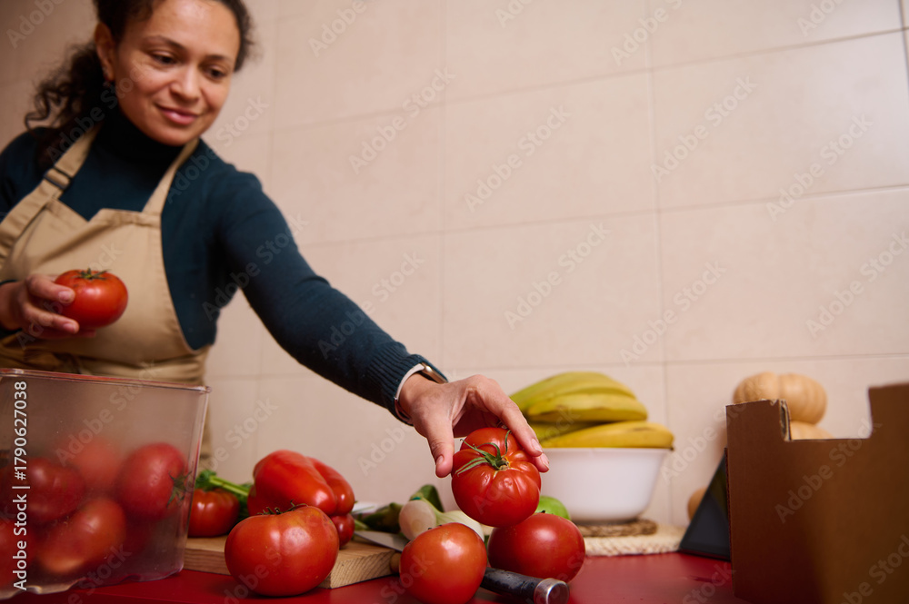 Fototapeta premium Woman In Apron Selecting Fresh Tomatoes In Kitchen For Cooking Or Market Prep
