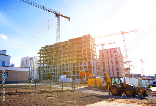 Construction site in modern urban area with cranes and machinery working. Heavy machinery working to erect new buildings. Tower crane on apartment construction. Block House building construction.