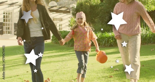 Walking family holding child wearing pink cap, carrying pumpkin pail on lawn with star overlays