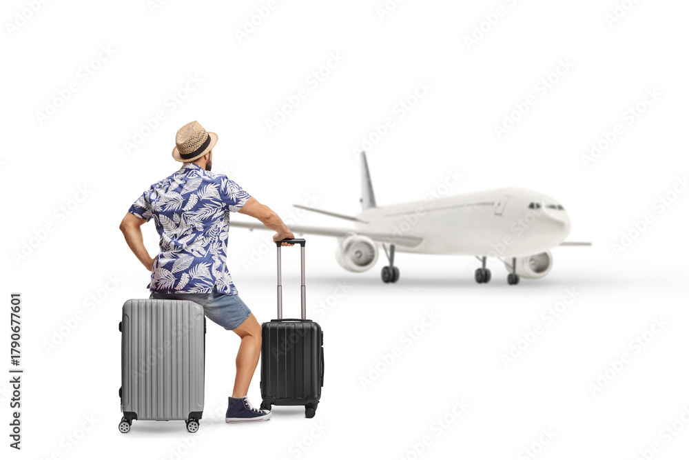 Obraz premium Rear view shot of a man sitting on a suitcase and looking at a plane