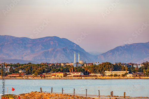 Fototapeta Naklejka Na Ścianę i Meble -  Sunset view of Side's coastline from the sea showing beaches, promenade, mosque with domes and minarets against forested mountains in golden evening light. Antalya, Turkey.

