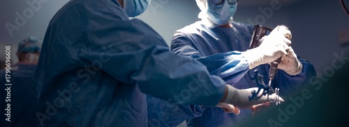 Surgeons in an operating room use robotic assisted technology for precision during knee replacement surgery. They wear surgical gowns, gloves, and masks in a sterile environment