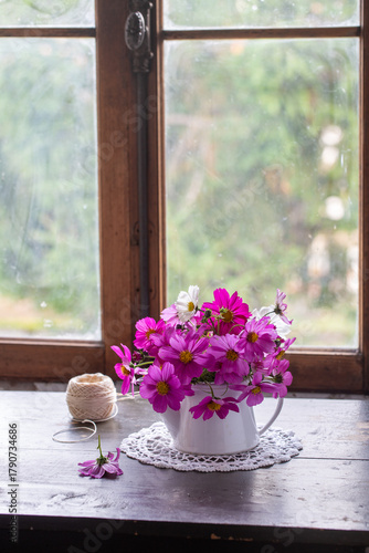 Vaso di ceramica con mazzo di fiori cosmea di colore rosa e bianco su un tavolo di legno di fronte a una finestra