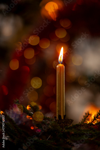 A golden candle burns on a Christmas tree.