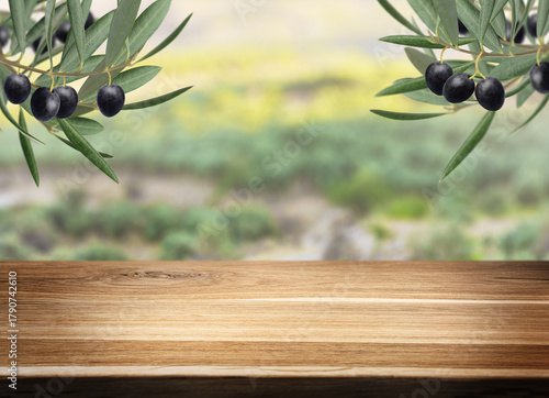 Fototapeta Naklejka Na Ścianę i Meble -  Fresh olive branch and rustic wooden table with copy space for product display over blurred landscape. Background for advertising and placement of natural and organic mediterranean food and oil