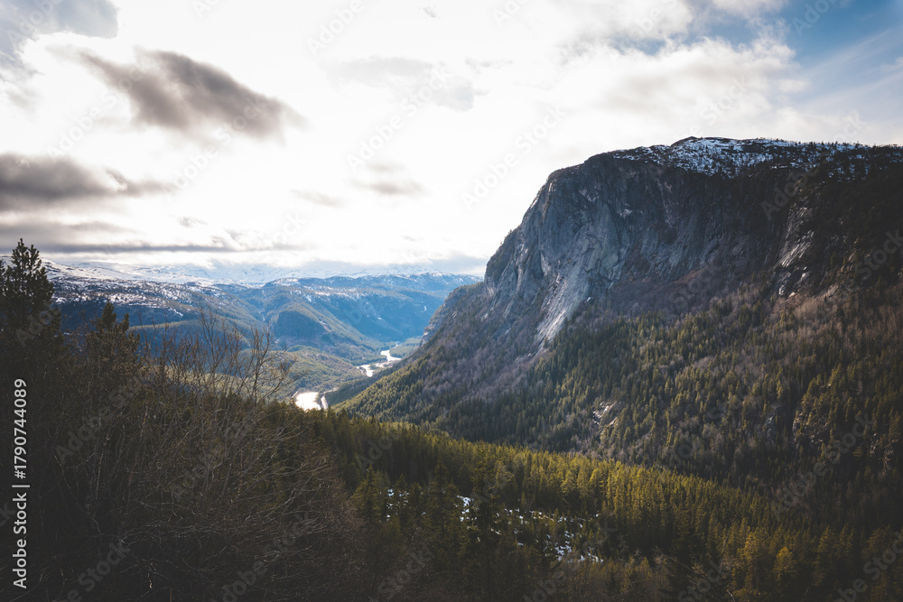 Fototapeta premium Epic mountain cliffs overlooking green valleys and snowy ridges in Norway. A cinematic view of Nordic wilderness and powerful nature