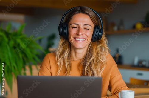 Happy woman smiling during online video meeting at home wearing headphones in creative workspace