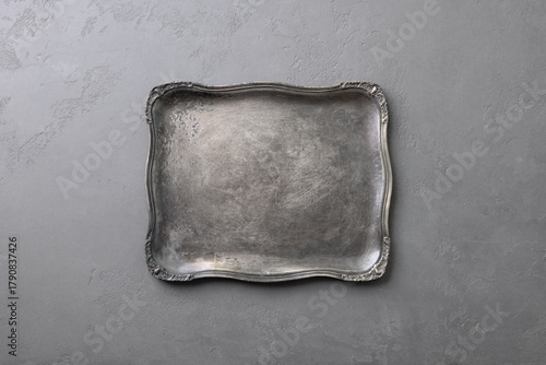 Elegant silver tray with ornate edges on textured gray background. Copy space. Top view.