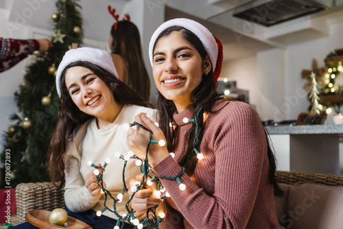 Latin woman Friends placing Christmas lights on Christmas tree at home in Mexico Latin America, hispanic people at holidays 