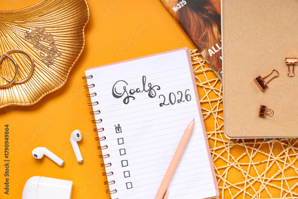 Naklejka premium Notebook with 2026 goals, earphones and accessories on orange background