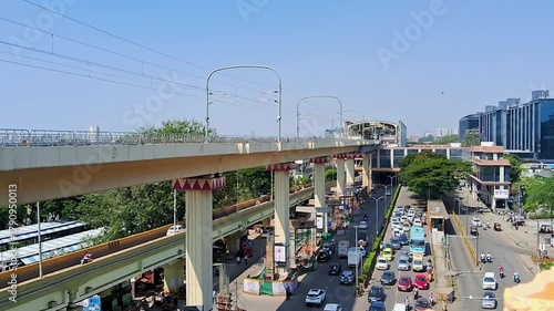 Elevated metro rail bridge above busy city road with modern buildings and vehicles during daytime