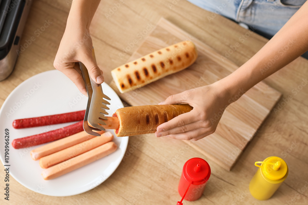 Obraz premium Young woman cooking hot dog in kitchen, top view