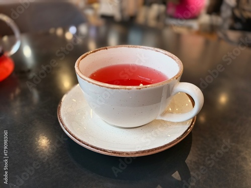 A rustic ceramic beige cup with bright red fruit tea is placed on a dark cafe table.