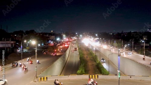 
Nighttime view of busy urban traffic on a multi-level flyover with cars, motorcycles, and a truck moving under bright streetlights.