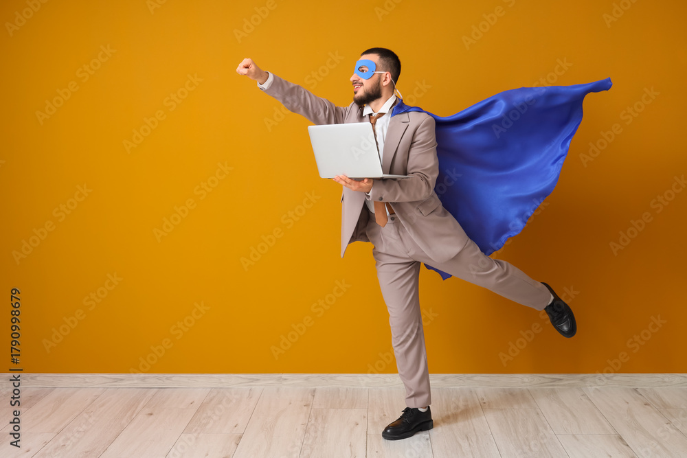 © Pixel-Shot - Young businessman dressed as superhero with laptop on orange background