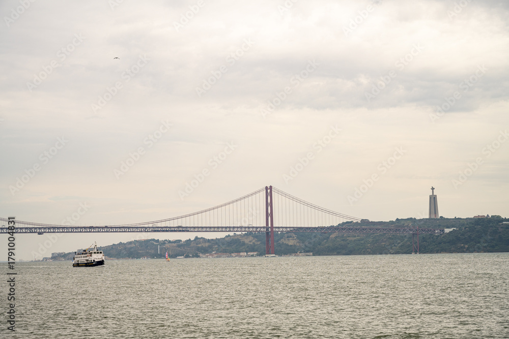 Naklejka premium Ferry boat on Tagus River with 25 de Abril Bridge and Christ the King monument Lisbon Portugal