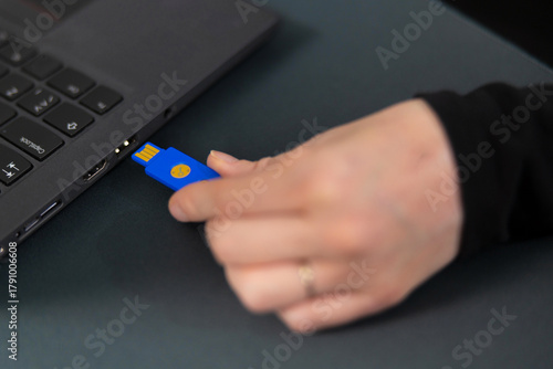 Female IT security technician in a tech office connects blue USB drive to a laptop