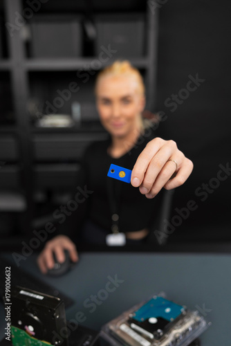 Female IT security technician holds blue USB drive in a tech storage workspace