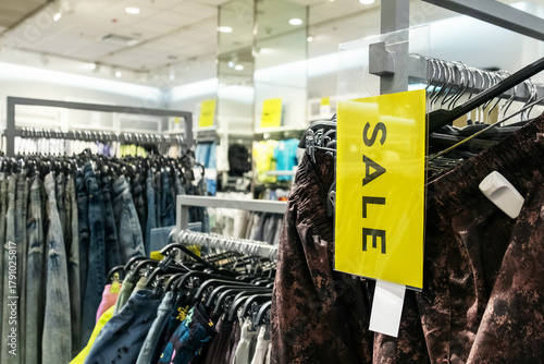 lothing racks with a prominent yellow sale sign show Black Friday discounts in a retail store. Shoppers can find fashionable trousers on offer during this seasonal shopping event.
