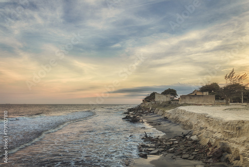 Old seaside houses on eroded coastline at sunset