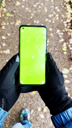 Person holding smartphone with green screen outdoors on autumn path