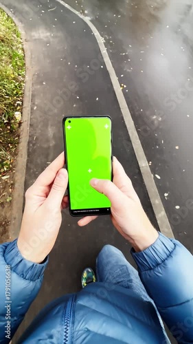 Top view of person walking on wet pavement holding smartphone with green screen
