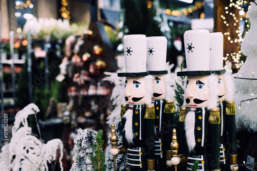 Wooden nutcracker soldier decorations in a Christmas market surrounded by lights, trees, and holiday decor. Christmas nostalgia, nutcracker tradition, vintage holiday decor, festive folklore