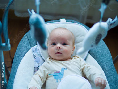 Newborn baby with bright blue eyes lying in cradle and curiously looking around. Newborn baby observes world with gentle expression. Newborn baby rests peacefully in calm cozy atmosphere.