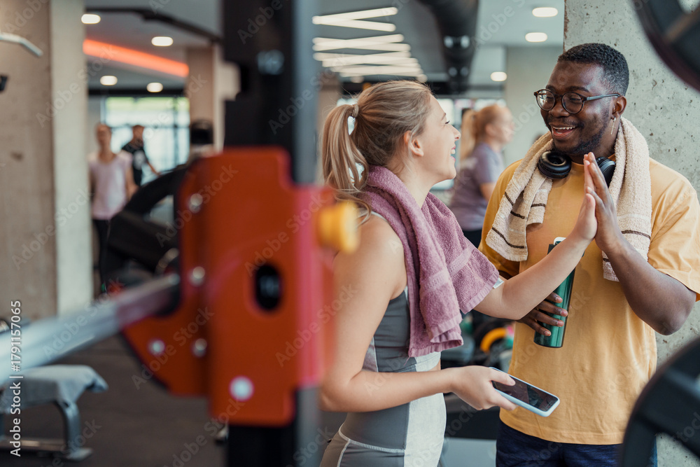Obraz premium Young adult woman and man exercising together smiling and high fiving in gym fitness center