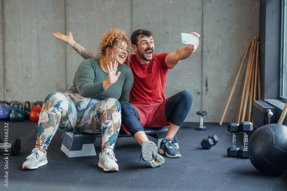 Fototapeta premium Bright indoor gym with diverse couple exercising together and taking a joyful selfie