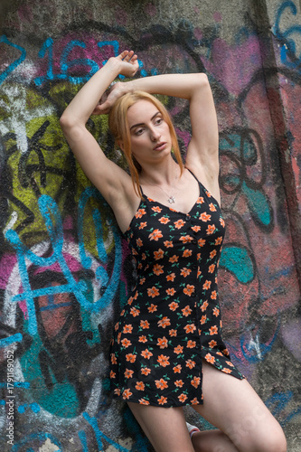 Blonde sensual woman with long legs posing confidently in front of a colorful graffiti wall, wearing a short floral dress. Urban fashion meets vibrant street art in this expressive portrait.