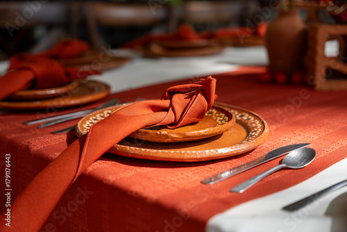 Wedding table in a rustic style, featuring artisan clay plates from Tonalá and Tlaquepaque, a red napkin, and white tablecloths with red accents. The decor blends event elegance with Mexican tradition